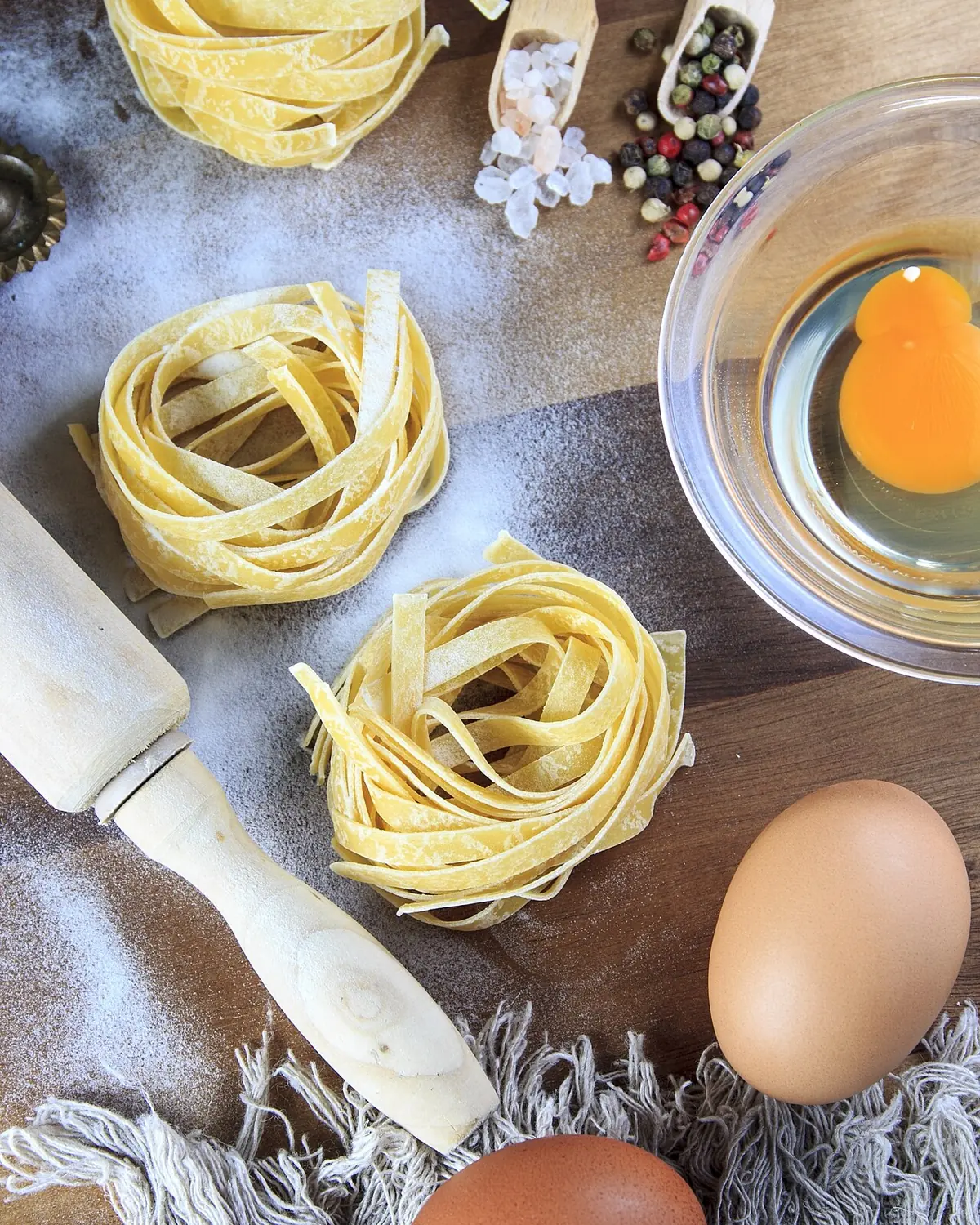 Tagliatelle fresche arrotolate accanto a un uovo e al mattarello